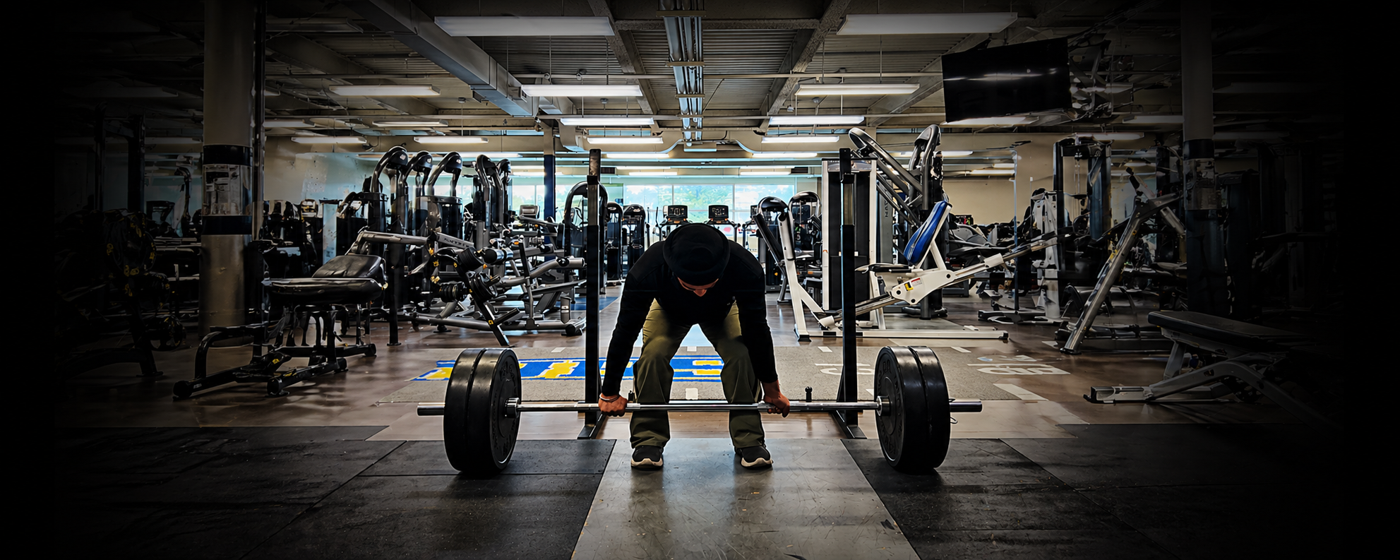 Karam setting up a barbell deadlift in a dimly lit gym